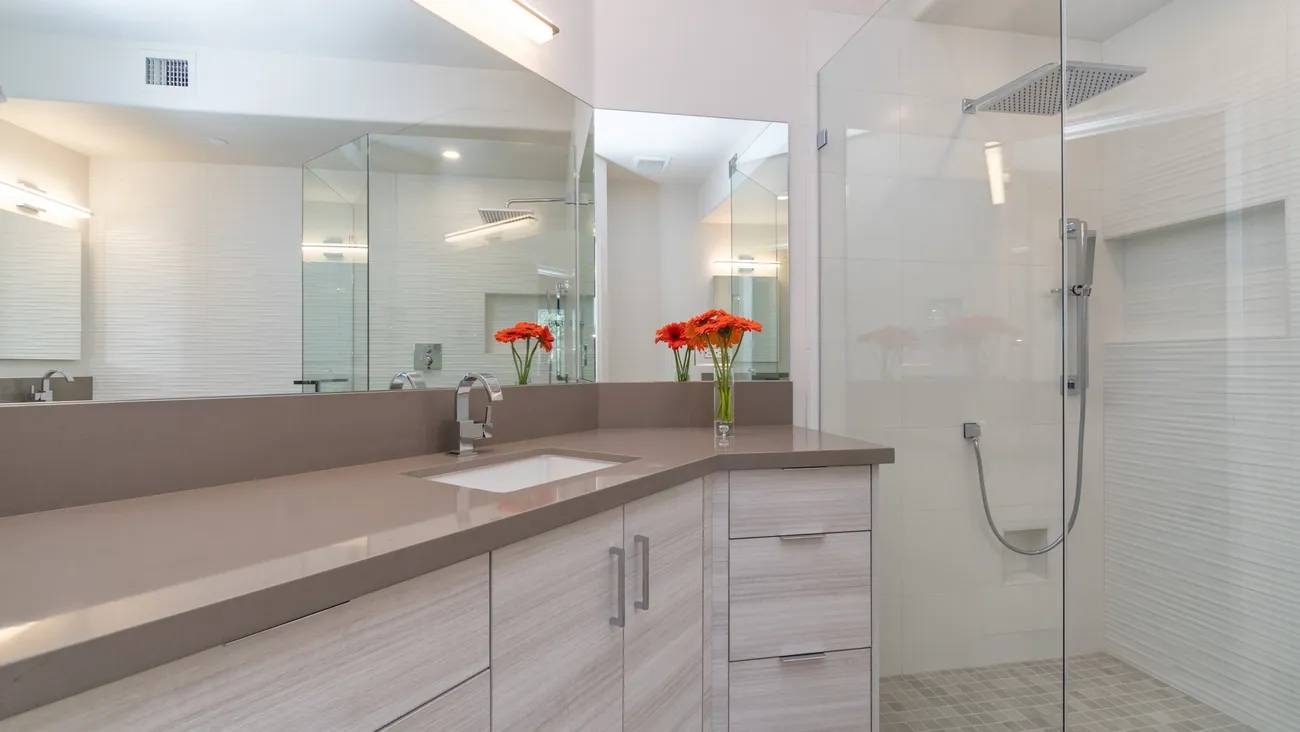 A bathroom with a sink, mirror and shower.