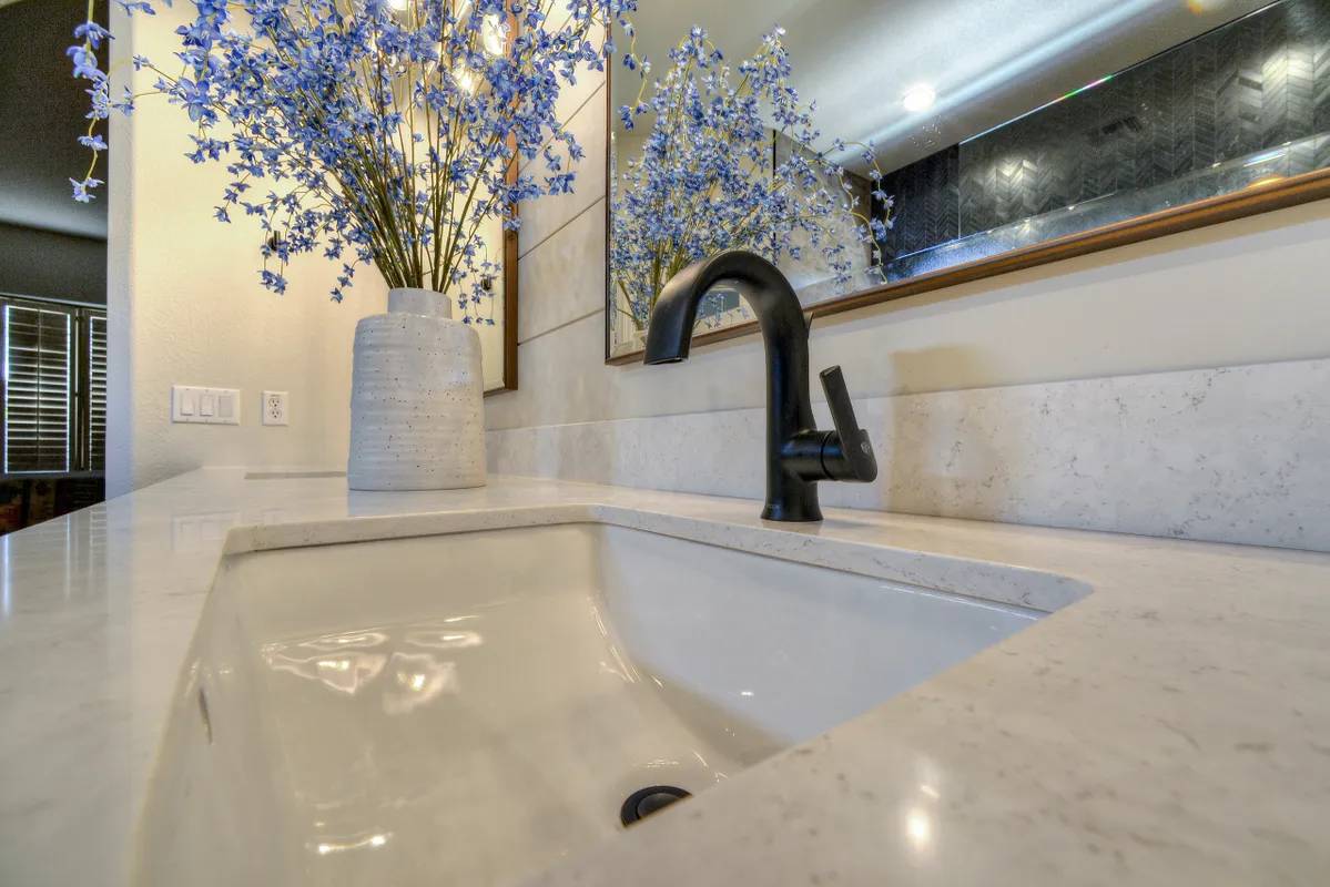 A bathroom sink with a mirror and flowers in the background.