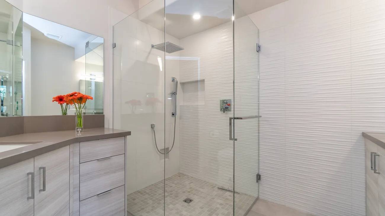 A bathroom with a large glass shower and white tile.