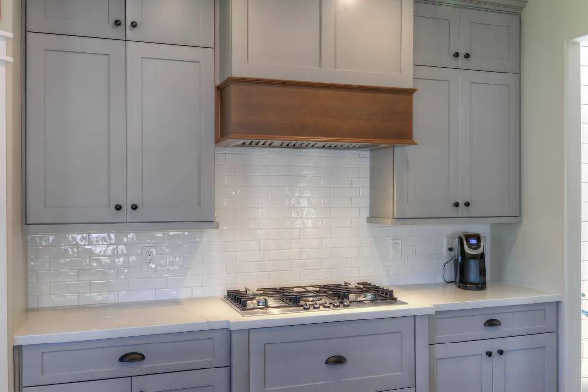 A kitchen with white cabinets and a wood hood.