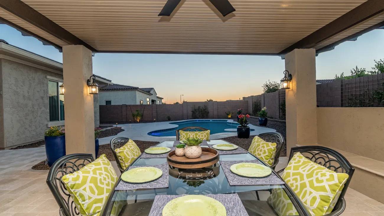 A patio with table and chairs, pool in the background.