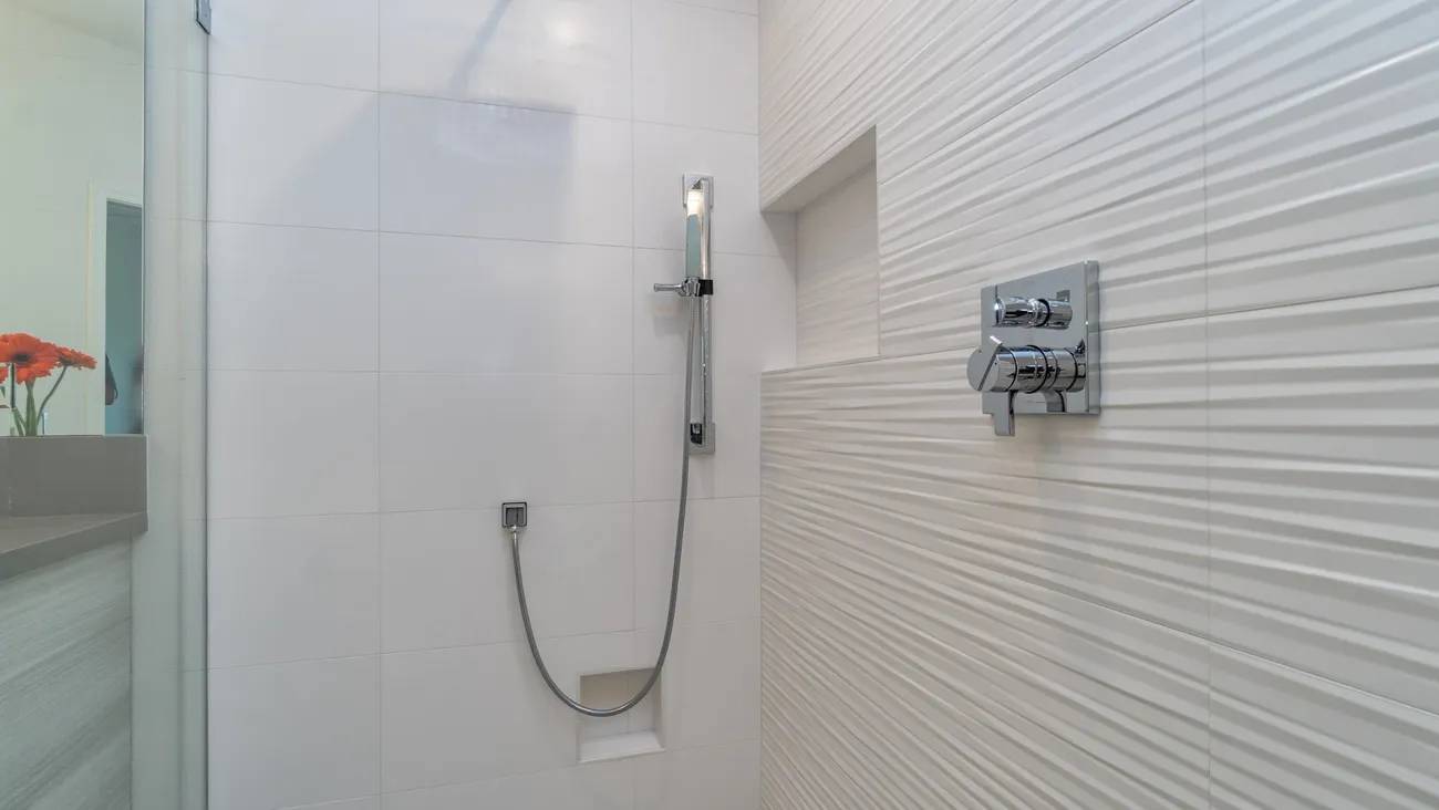 A shower with white tile and a silver fixture.