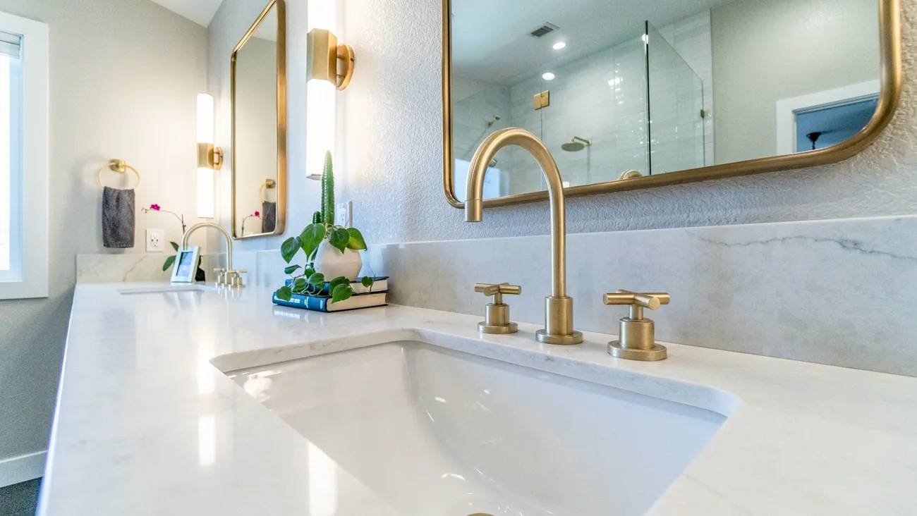 A bathroom sink with gold fixtures and a mirror.