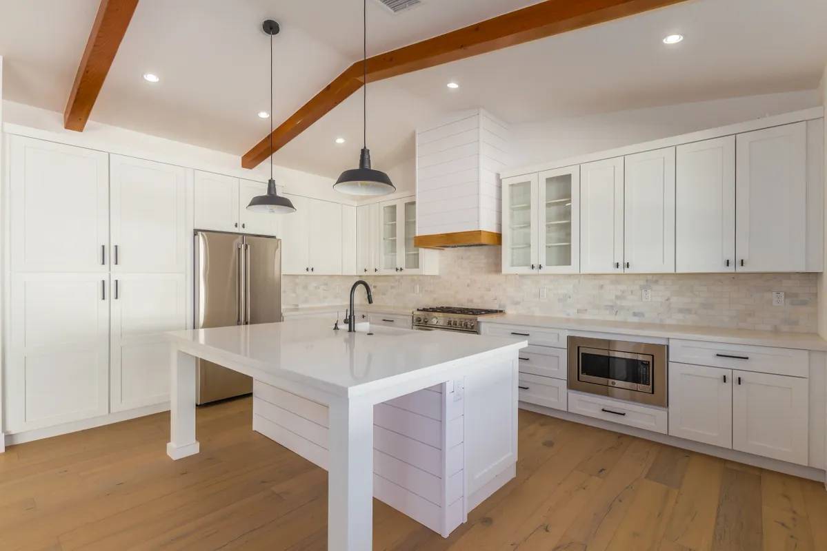 A kitchen with white cabinets and wood floors.