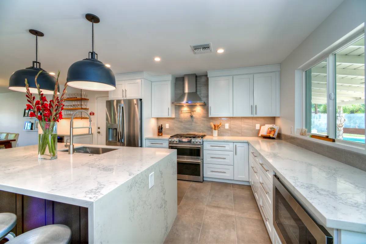 A kitchen with white cabinets and marble counter tops.