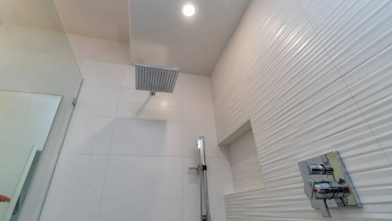 A bathroom with white tile and a shower head.